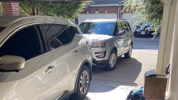 Eine Garage mit zwei Autos darin. Kartons und verschiedene Gegenstände sind verstreut.