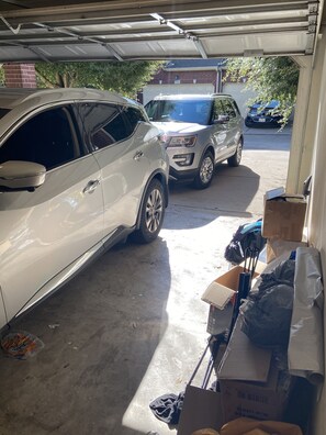 Eine Garage mit zwei Autos darin. Kartons und verschiedene Gegenstände sind verstreut.