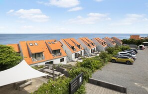 Eine Reihe moderner Gebäude mit orangefarbenen Ziegeldächern, ein Parkplatz und Meerblick.