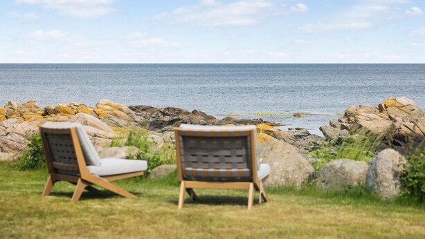 Deux fauteuils confortables sont placés face à un rivage rocheux, offrant une vue sur la mer.