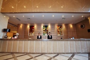 A hotel reception area with a marble counter, two receptionists, and large framed artwork on the wall. - Faguo Hotel (Dalian)