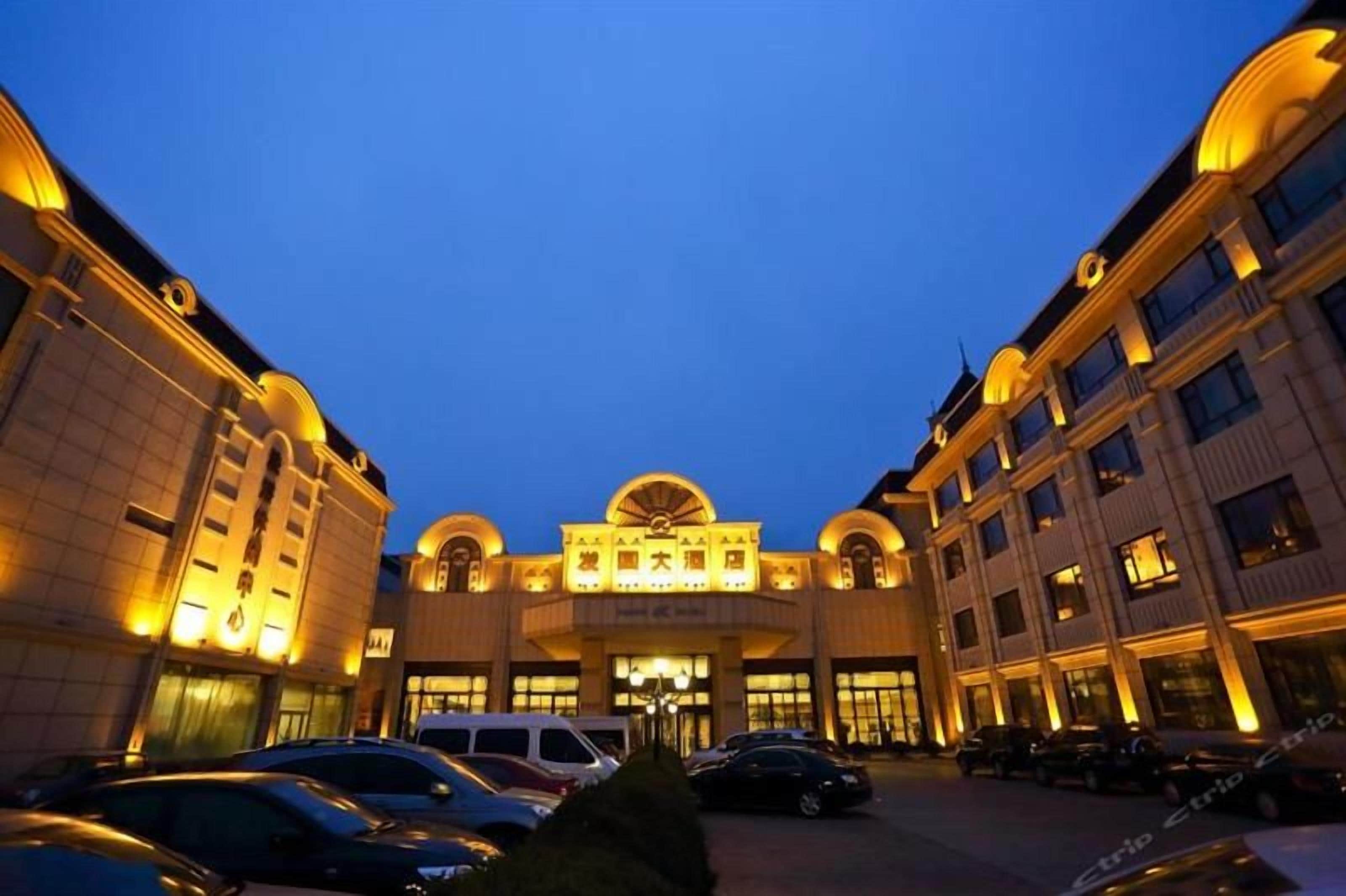 A hotel with a central entrance, multiple floors, and a parking area with cars.