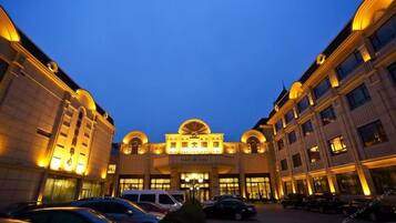 A hotel with a central entrance, multiple floors, and a parking area with cars.