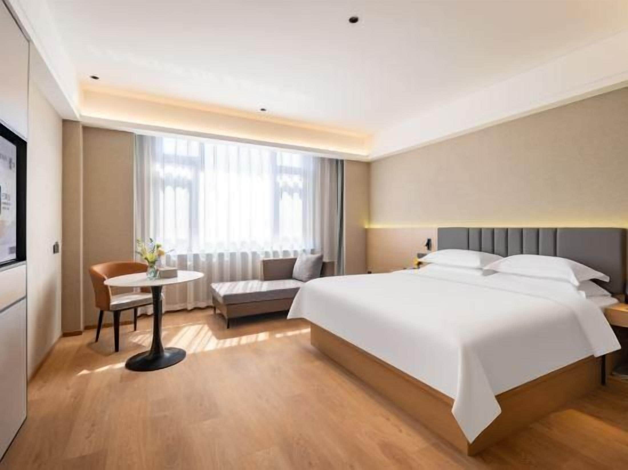 Una habitación de hotel con una cama, un escritorio, una silla y un ventanal con cortinas.