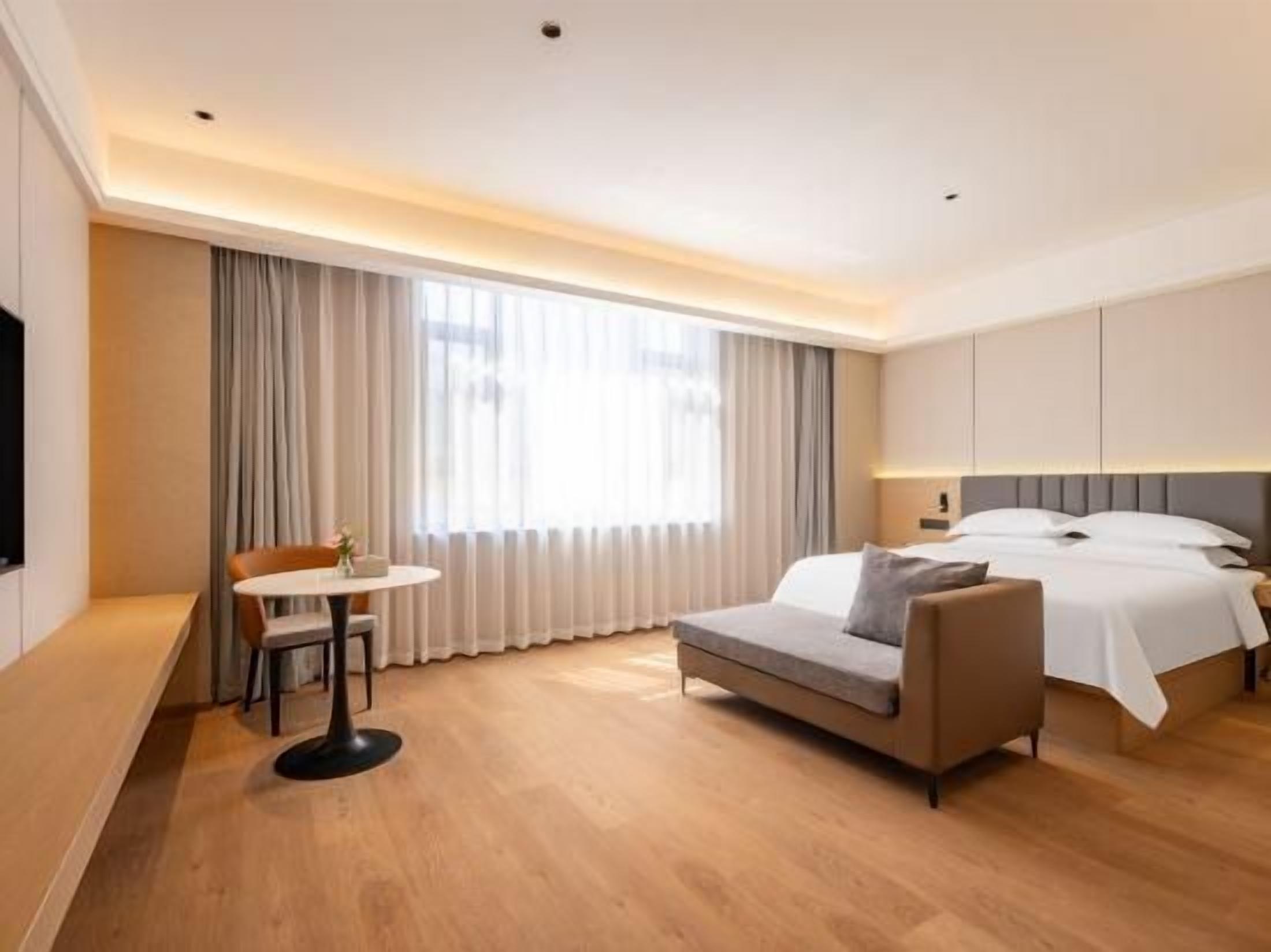A hotel room with a bed, a sofa, a small table, and a TV.