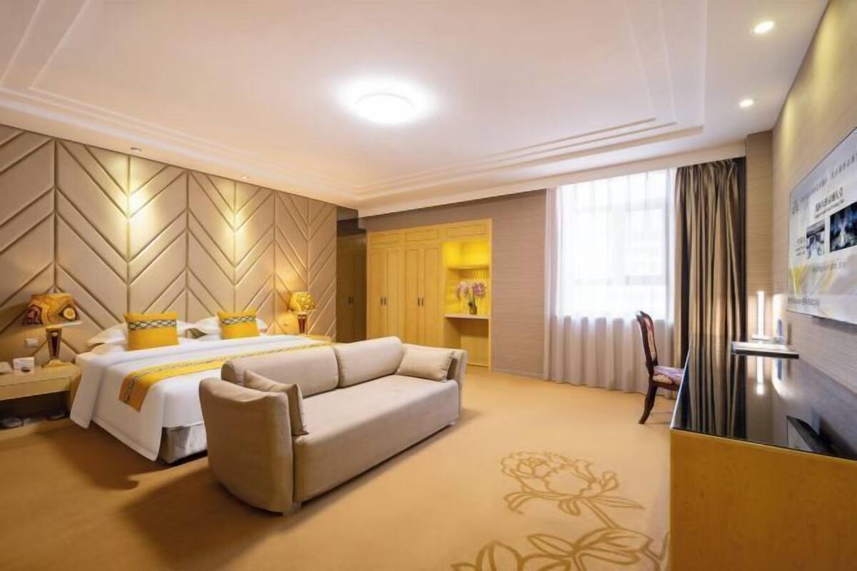 Una habitación de hotel con cama, sofá, escritorio y un ventanal con cortinas.