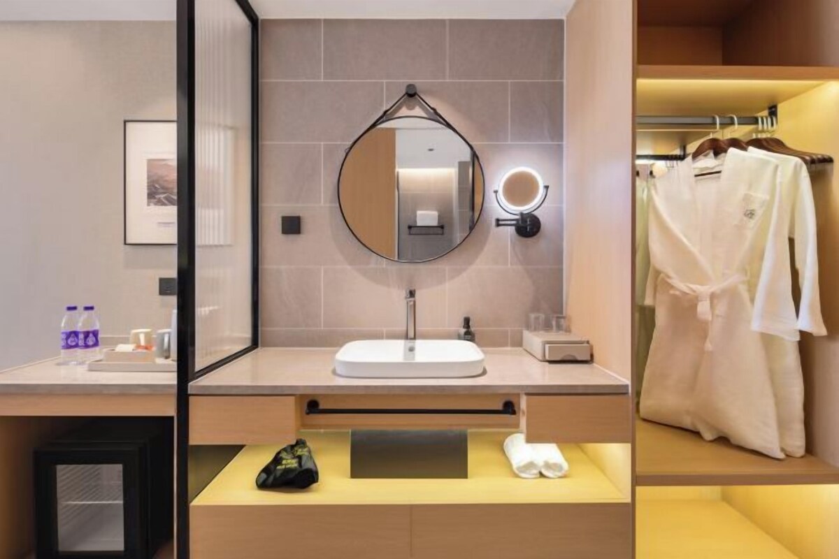 A modern bathroom with a round mirror, a sink, and a towel rack with white robes.