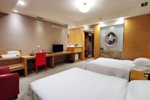 A hotel room with two beds, a desk with a computer, a red chair, and a wardrobe.