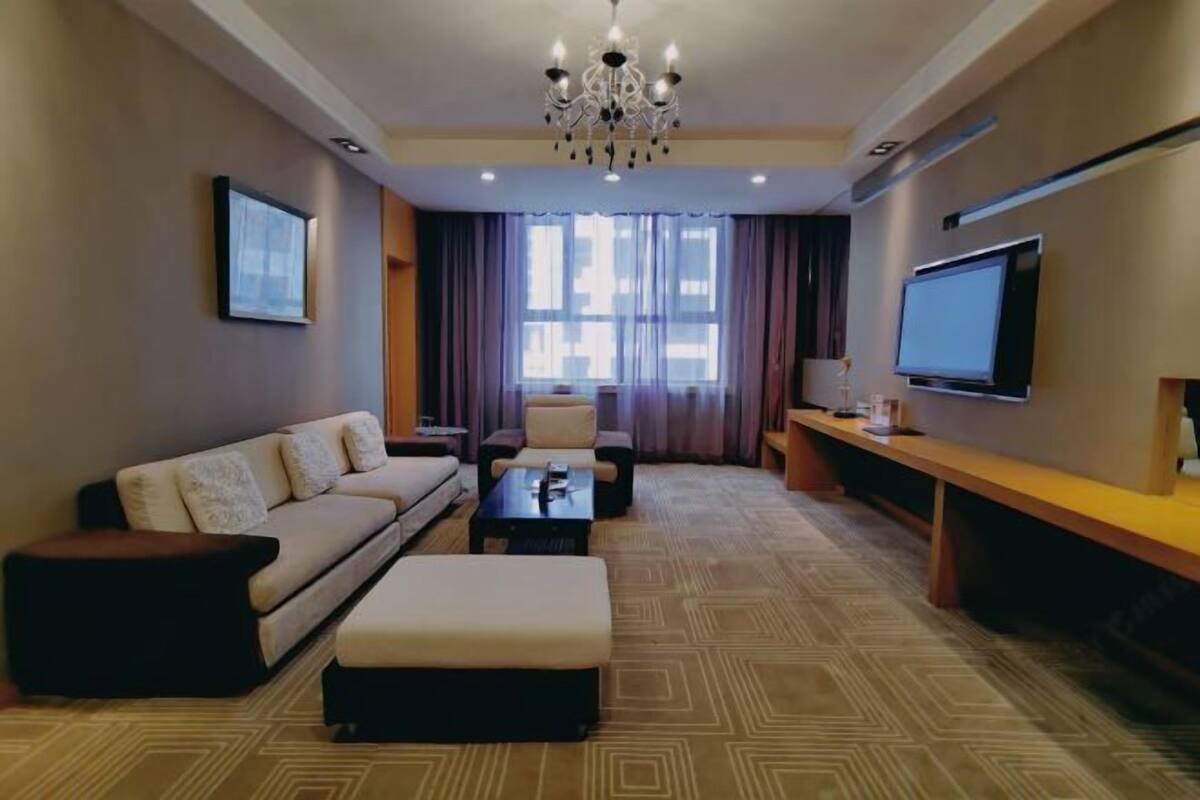 Una sala de estar moderna con sofá, reposapiés, mesa de centro, televisor y una araña.