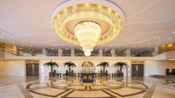 A spacious lobby with a large circular chandelier, palm trees, and a central decorative fountain. - Faguo Hotel (Dalian)