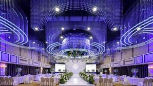 A banquet hall with a central aisle, rows of round tables, and a ceiling with a geometric light design. - Faguo Hotel (Dalian)