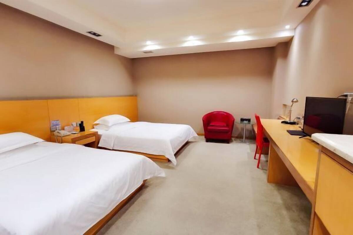 Habitación de hotel con dos camas, un escritorio, un televisor y una silla roja.