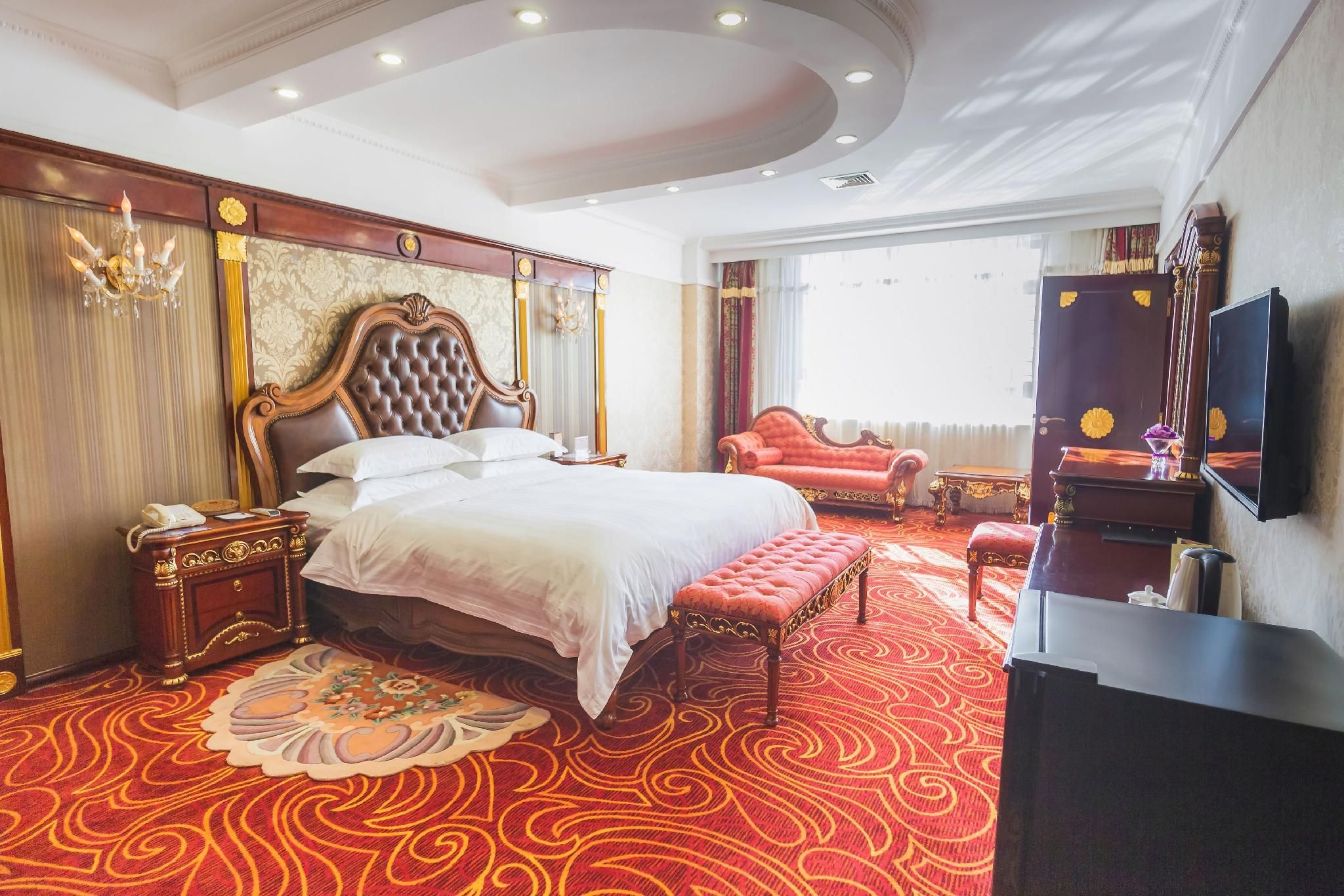 Una camera d'albergo con un letto grande, un'area salotto con un divano rosso, una televisione e un tappeto decorativo.