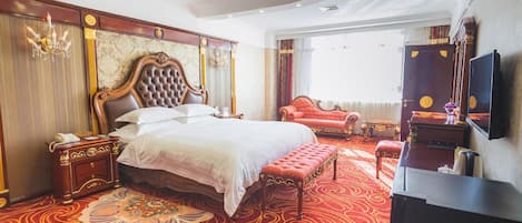 A hotel room with a large bed, a sitting area with a red sofa, a television, and a decorative rug.