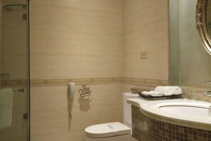 A bathroom with a toilet, a sink, a mirror, and a shower area. - Faguo Hotel (Dalian)