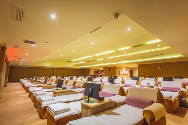A room with multiple massage therapy beds arranged in rows, each with a control panel and a small table.