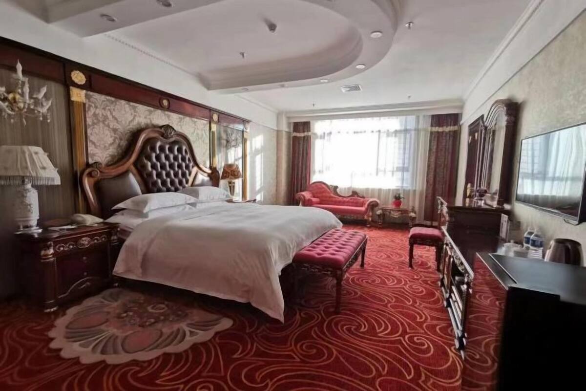Una habitación de hotel con una cama grande, una alfombra roja, un televisor y una araña.