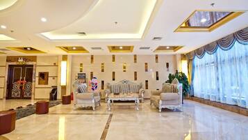 A spacious lobby with a high ceiling, ornate furniture, and a large window with curtains.