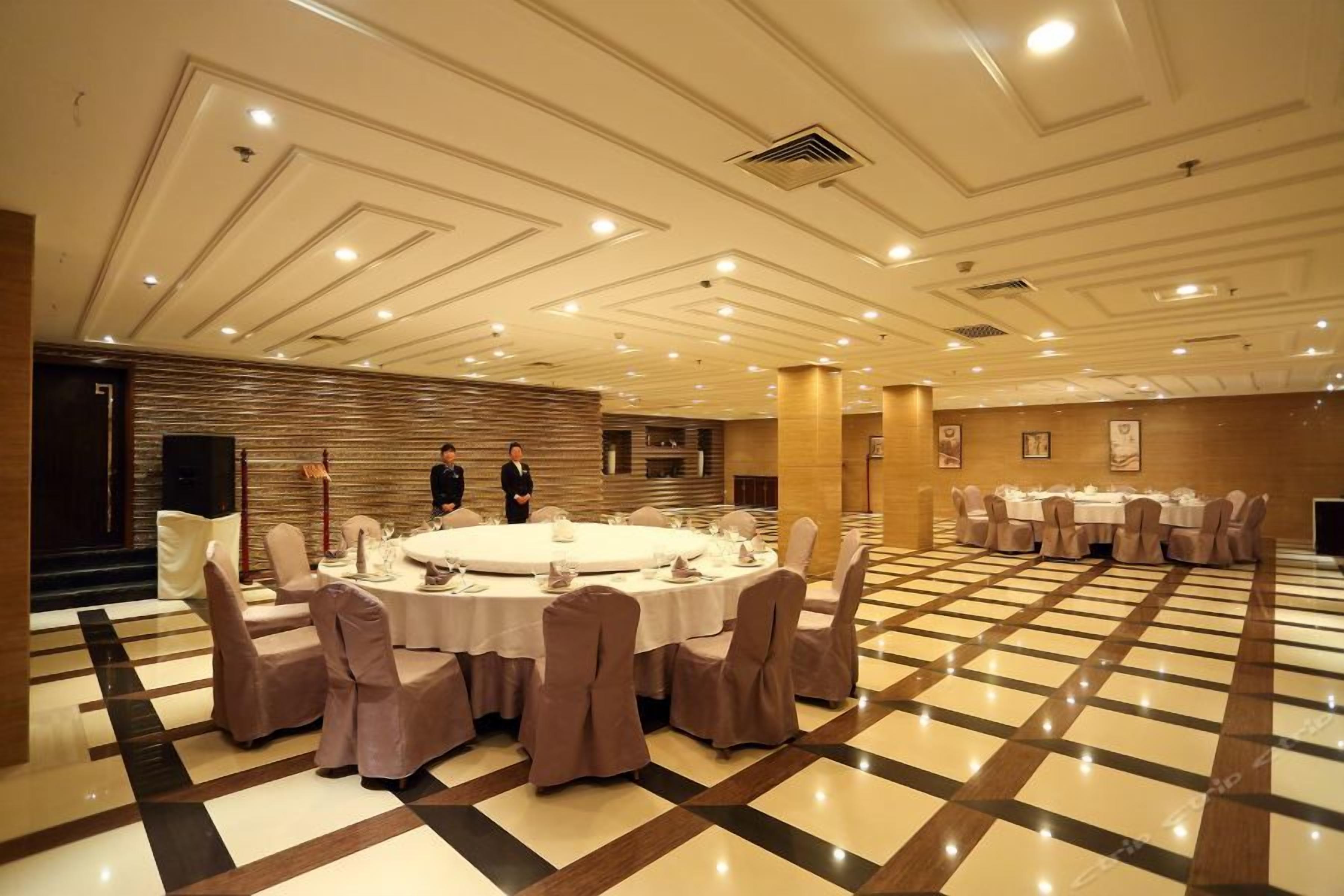 A banquet hall with round tables set for dining, a checkered floor, and a modern ceiling design.