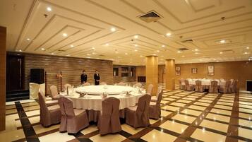 A banquet hall with round tables set for dining, a checkered floor, and a modern ceiling design.