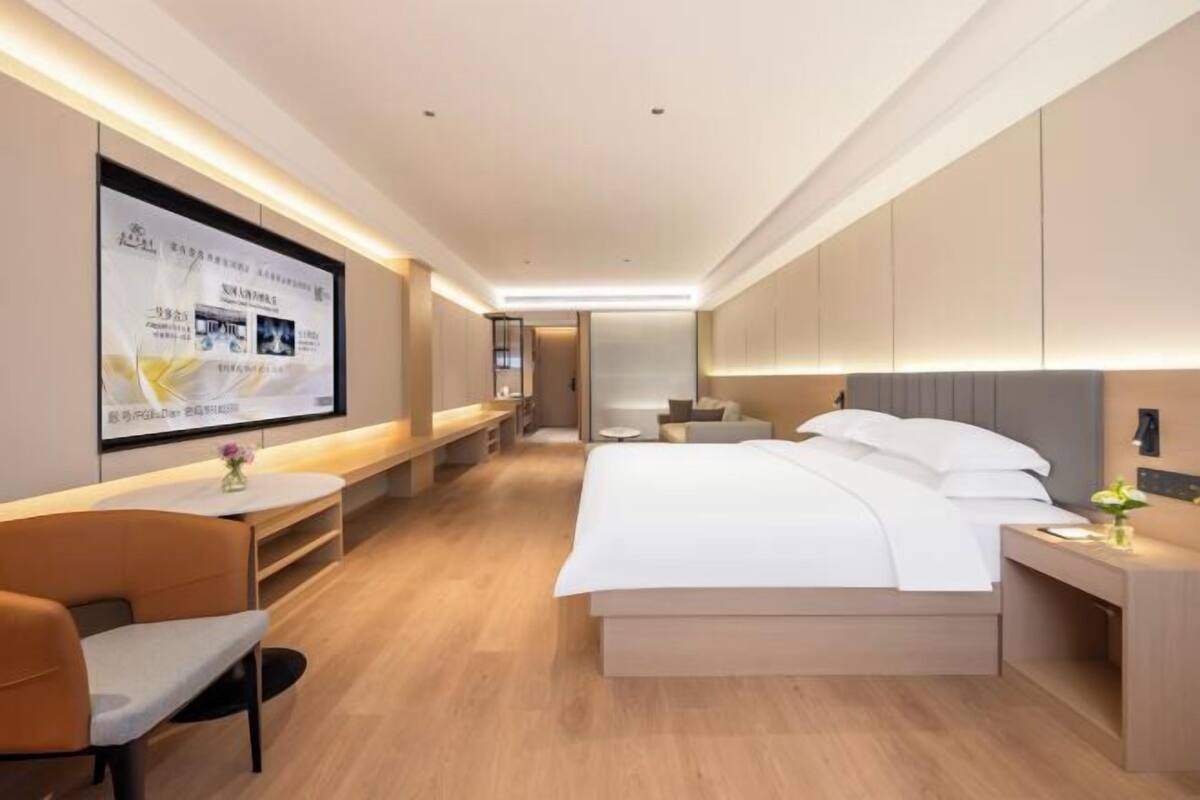 Una habitación de hotel moderna con cama, mesita de noche y una zona de estar con una silla y una mesa.