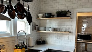 A modern kitchen with white tiled walls, stainless steel appliances, and black cabinets. There are hanging pots, a dish rack, and a box of beer on the counter. - The Kohler House (Kohler)