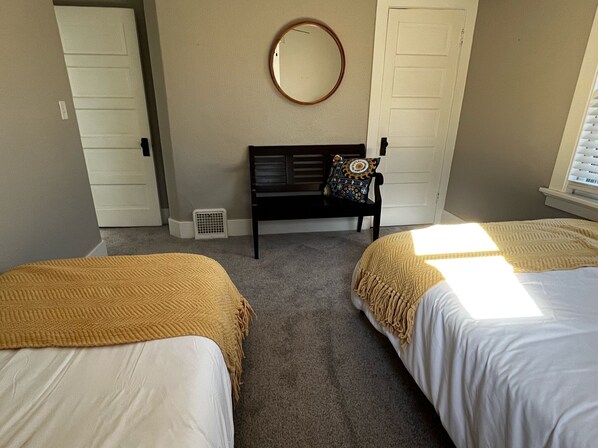 Ein Schlafzimmer mit zwei Betten, einer Bank mit Kissen, einem runden Spiegel an der Wand und einer Tür.