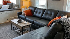 A modern living room with a black leather sofa, a wooden coffee table, and a window with blinds. - The Kohler House (Kohler)
