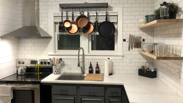 A kitchen with white tiled walls, a stainless steel stove, a sink, and a window above the countertop. - The Kohler House (Kohler)