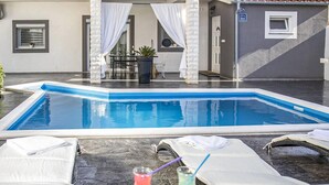 Ein Pool mit Liegestühlen und Getränken, ein Tisch mit Stühlen und ein Gebäude im Hintergrund.
