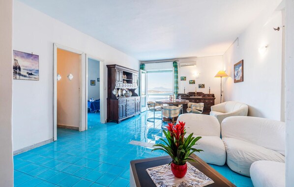 A spacious living room with a blue-tiled floor, a white sofa set, a dining area with a table and chairs, and a view through a glass door. - Cozy apartment in Ischia with WiFi (Ischia)