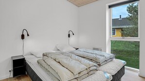 A bedroom with a bed, bedside tables, and a window with a view of a house and greenery.