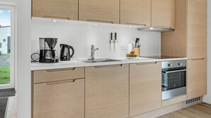 A modern kitchen with light wood cabinets, a stainless steel sink, a coffee maker, and an oven.