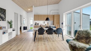 A modern kitchen with wooden cabinets, a dining area with a table and chairs, and a large sliding glass door leading to a balcony.
