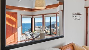 A modern room with large windows, a dining area, and a view of the sea. - Coastal Luxury: Oceanfront Views, Decks + Walkable to Downtown (Monterey)