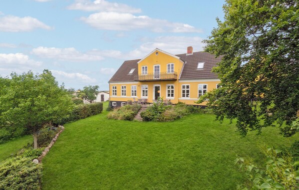 Une maison jaune avec un balcon, entourée d’une pelouse bien entretenue et d’arbres.