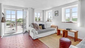 A bright room with a white sofa, a wooden bench, and a view of the outdoors through large windows. - Gorgeous apartment in Nexø with WiFi (Nexø)