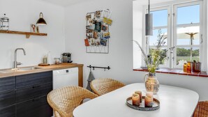 A modern kitchen with a white countertop, stainless steel sink, and a dining area with wicker chairs and a white table. - Gorgeous apartment in Nexø with WiFi (Nexø)