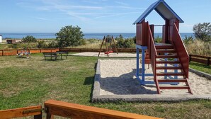 A beachside playground with a slide and swings, surrounded by a wooden fence and a picnic table. - Gorgeous apartment in Nexø with WiFi (Nexø)