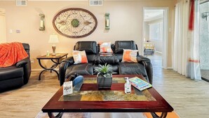 A living room with a black leather sofa, a coffee table with a plant, and a decorative wall piece. - Lakefront Action | Paddle • Pickle • Pool • Sunset (Montgomery)