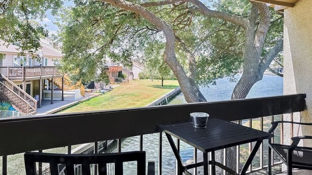 A balcony with a view of a lake, a wooden deck, and a staircase leading to a building. - Lakefront Action | Paddle • Pickle • Pool • Sunset (Montgomery)