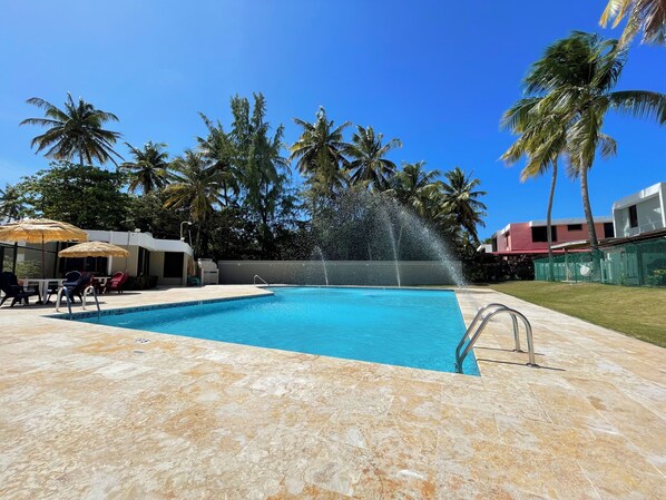 A swimming pool with a water fountain, lounge chairs, and palm trees in the background.