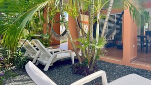 Un espacio al aire libre tropical con sillones blancos, una hamaca y exuberante follaje.
