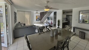 Una sala de estar moderna con un sofá gris, una mesa de comedor con sillas, una escalera y una zona de cocina.