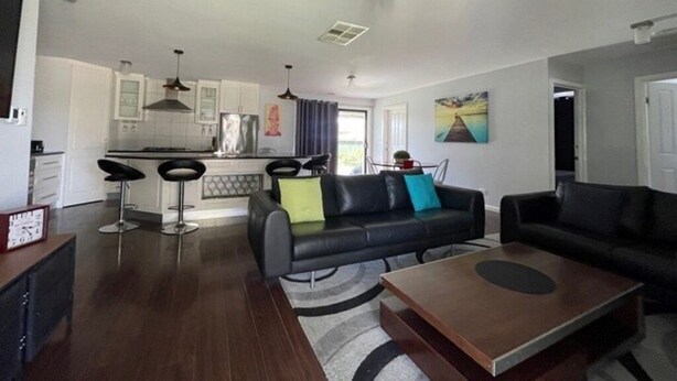 A modern living room with a black leather sofa, a wooden coffee table, and a kitchen area with white cabinets and a dining table. - Aqua Vista  – Family friendly accommodation right in the heart of Yarrawonga. (Yarrawonga)