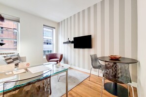 Un salon moderne avec une table basse en verre, un fauteuil rouge, une table ronde sur laquelle est posé un saladier, un téléviseur fixé au mur et un mur à rayures.