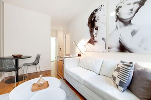 Una sala moderna con un sofá blanco, una mesa de centro de vidrio y una zona de comedor con una mesa y sillas negras.