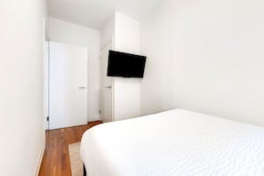 A bedroom with a bed, a flat-screen TV mounted on the wall, and a wooden floor.