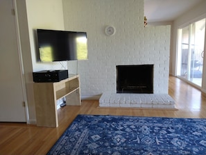 A living room with a flat-screen TV mounted on the wall, a white brick fireplace, wooden flooring, and a blue patterned rug. - 3 Bed 2 Bath House San Mateo Next to Lagoon (San Mateo)