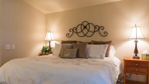 Une chambre à coucher avec un grand lit, deux lampes de chevet, un élément décoratif mural et une table de chevet avec une lampe et une boîte à mouchoirs.